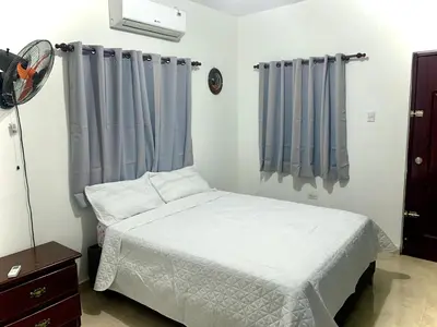 a bedroom with a white bed and blue curtains at Casa Linda - 10 mins from Beach & Lagoon with AC & Free Parking in Payita