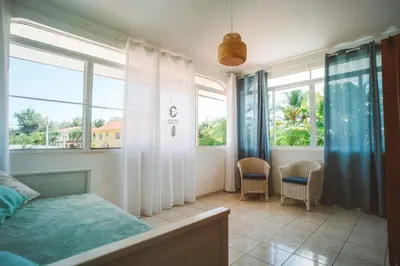 a bedroom with a bed and two chairs and windows at Sueño Caribeño in La Laguna