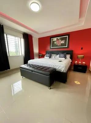 a bedroom with a large bed with a red wall at Luxury 5 Beds Penthouse - Private Jacuzzi & Karaoke Bar & Free Parking in Santiago de los Caballeros