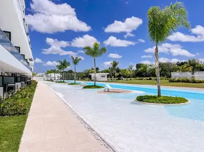 a large swimming pool with a palm tree next to a building at Luxury Apartment at Cana Rock Star Punta Cana DR in Punta Cana