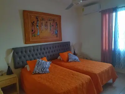 two beds with orange sheets in a room with a window at Condo Penthouse Batey Dominicus in Bayahibe