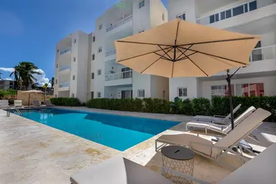 a pool with a chair and an umbrella next to a building at Arena Village | 2H Retiro con Vista a Piscina in Punta Cana