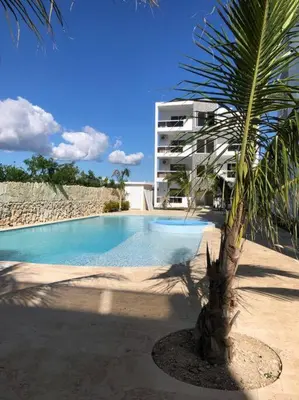 a palm tree in front of a building with a swimming pool at Sol Caribe 101 Bayahibe con linda piscina! in Bayahibe