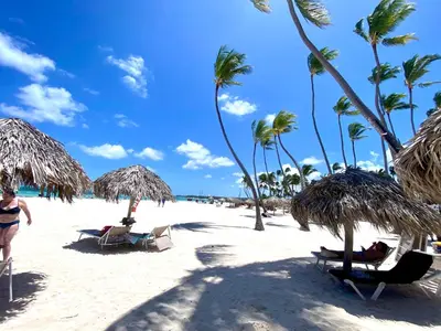 a beach with chairs and umbrellas and palm trees at Madonna1 pool beach los corales Arenas de Bavaro in Punta Cana