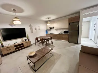 a living room with a table and a kitchen at Komfortowy Apartament z 4 Basenami i Pięknym Ogrodem, Estrella Dominicus-Bayahibe in Bayahibe