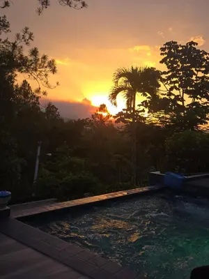 a sunset over a swimming pool with a palm tree at Luxury Mountain villa, Jarabacoa villa vargas in Concepción de La Vega