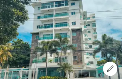 a tall white building with palm trees in front of it at Condo Apartment in Ciudad Nueva