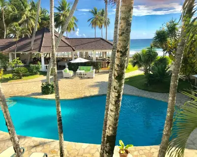 a resort pool with palm trees and the ocean at Surf and Yoga Retreat for Groups Near Cab! in Gaspar Hernández