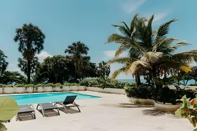 a swimming pool with two chairs and palm trees at Oceanfront 3 Bedroom With Jacuzzi and Pool in Santo Domingo