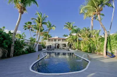 a swimming pool in front of a house with palm trees at TRACADERO Beach Club & Holidays Rentals in Bayahibe