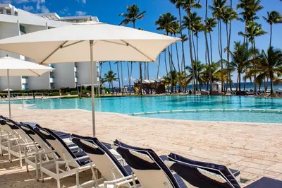 a swimming pool with chairs and an umbrella at Marbella Juan Dolio Beachfront in Juan Dolio