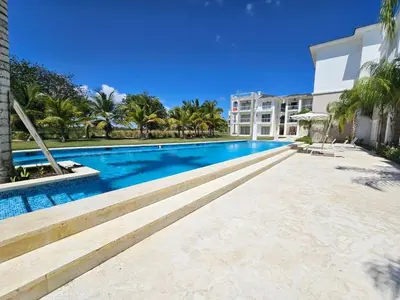 a swimming pool with palm trees and a building at Comfort Condo w/Pool View at Hard Rock Golf Course in Punta Cana