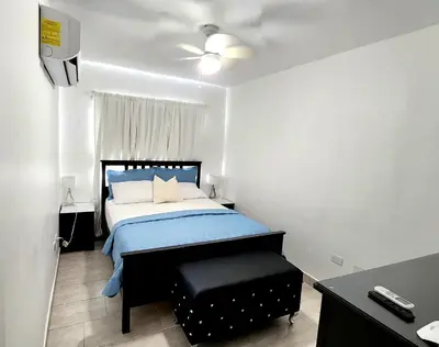 a bedroom with a bed and a black ottoman at Apartamento Riviera Colonial, Santo Domingo in Calero