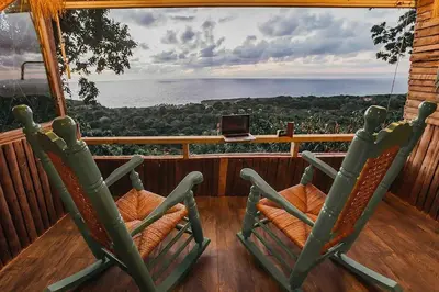 two green rocking chairs on a porch with a view at Casa El Paraiso, Eco Lodge in Santa Bárbara de Samaná