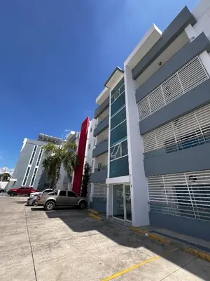 two buildings with cars parked in a parking lot at Bello Apartamento en Santiago con todas las comodidades in Santiago de los Caballeros