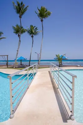 a bridge leading to the beach with palm trees at Xeliter Las Olas Juan Dolio in Guayacanes