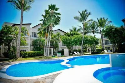 a swimming pool in front of a building with palm trees at Punta Cana 1-Bed Apt Sleeps 4 with Pool & Hot Tub in Punta Cana