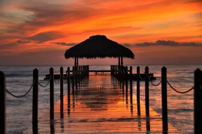a pier with a straw umbrella and the ocean at sunset at Apartment in Cadaques Caribe in Bayahibe