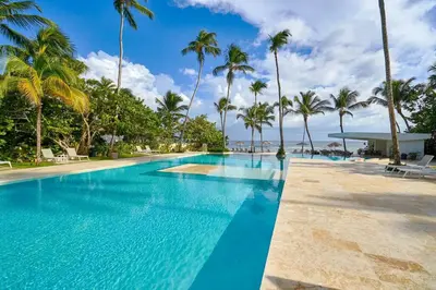 a swimming pool with palm trees and the ocean at Aquarella Sunset Caribbean Beachfront Gataway in La Puntica de Juan Dolio