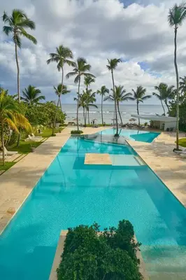 a large swimming pool with palm trees and the ocean at Aquarella Sunset Caribbean Beachfront Gataway in La Puntica de Juan Dolio