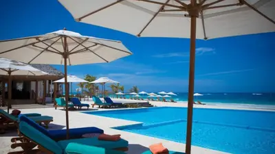 a swimming pool with chairs and umbrellas and the ocean at Cana Rock Condos in Punta Cana