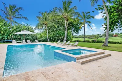a pool with chairs and an umbrella and palm trees at Gorgeous villa at Casa de Campo - with large pool, cook, maid and 2 golf carts in La Romana
