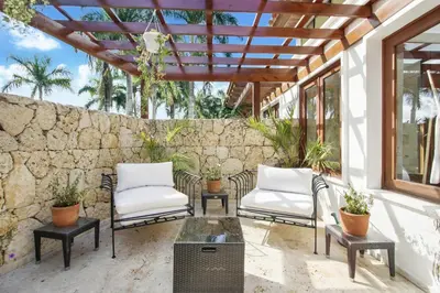 a patio with white chairs and a stone wall at Gorgeous villa at Casa de Campo - with large pool, cook, maid and 2 golf carts in La Romana