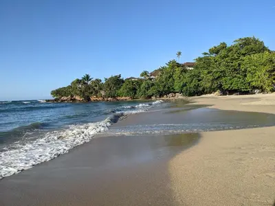 a sandy beach with a body of water and trees at 1BR Suite at Villa Costa Verde near Playa Cofresi, Puerto Plata, with a pool, balcony and a rooftop terrace in San Felipe de Puerto Plata