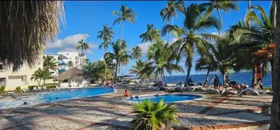 a resort swimming pool with palm trees and the ocean at Apartamento ll Vista al Mar Albatros BY JU Juan Dolio in Juan Dolio
