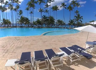 a pool with chairs and palm trees on a beach at Beachfront Apartment with Jacuzzi in Juan Pedro