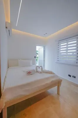 a white bedroom with a large bed with a window at Villa Hermosa en Metro Country Club Juan Dolio in Juan Dolio
