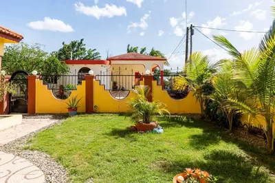 a yellow house with a yard with palm trees at Casa para vacacionar - El patio de Olivia in San Felipe de Puerto Plata