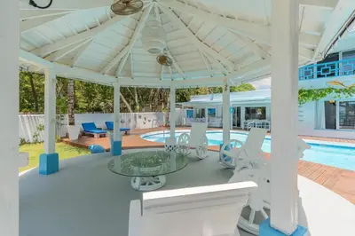 a white pavilion with a table and chairs and a pool at Dolce Casa in Juan Dolio