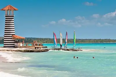 a beach with a lighthouse and people swimming in the water at Estrella Dominicus - Excepcional Apartamento en el Caribe in Bayahibe