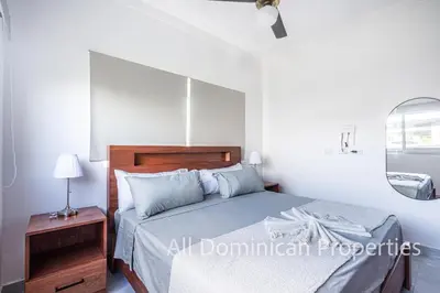 a white bedroom with a bed and a night stand at Villas Santa Fe in Sosúa