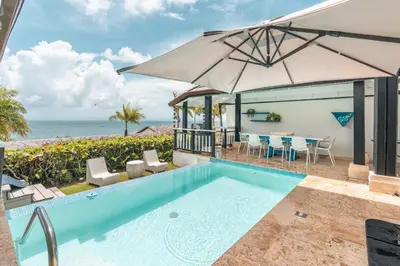 a swimming pool with an umbrella and the ocean at Magnificent villa with ocean view in Puerto Bahia in Sabana