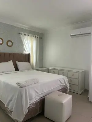 a white bedroom with a large bed with a stool at Apartamento con Deslumbrante Vista Al Mar in La Francia