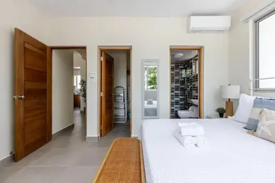 a white bedroom with a large bed and a bathroom at Caribey 2, Las Terrenas in Las Terrenas