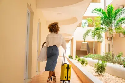 a woman walking down a hallway with a yellow suitcase at Hotel El Imperio Punta Cana in Punta Cana