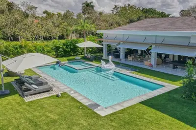 a swimming pool with two umbrellas and a house at Villa Pradera, Upscale Comfort In Casa De Campo in La Romana