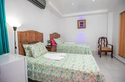 a hotel room with two beds and a chair at Casa de Huespedes Colonial in Santo Domingo