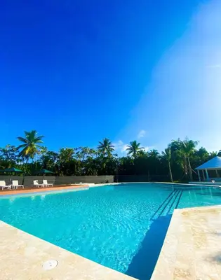 a swimming pool with blue water and palm trees at Apartamento de playa in San Felipe de Puerto Plata
