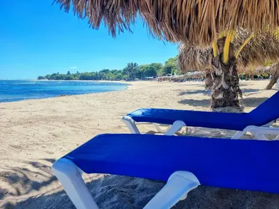a blue beach chair sitting under a straw umbrella at Costambar Ocean Breeze - Beachfront Apartment with Pool in San Felipe de Puerto Plata