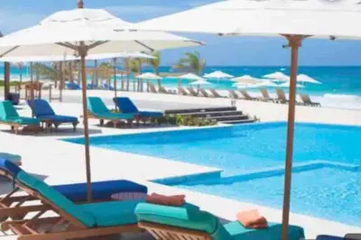 a swimming pool with chairs and umbrellas and the ocean at The Peña family suite in Punta Cana