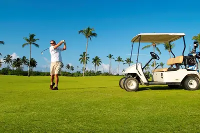 a man is playing golf next to a golf cart at Bahia Principe Luxury Bouganville - Adults Only All Inclusive in La Romana