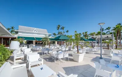 a patio with white tables and chairs and palm trees at Bahia Principe Grand El Portillo - All Inclusive in Las Terrenas