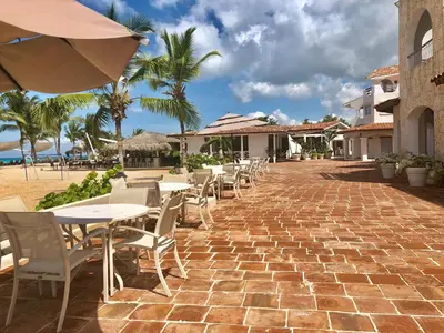 an outdoor patio with tables and chairs and palm trees at Beach Day at CadaquesCaribe Bayahibe in Bayahibe