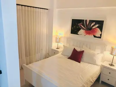 a white bedroom with a white bed with two lamps at Hermoso Apartamento cerca de la playa, Restaurantes, Supermercados, Restaurantes, Aeropuertos, parqueo gratis in Boca Chica