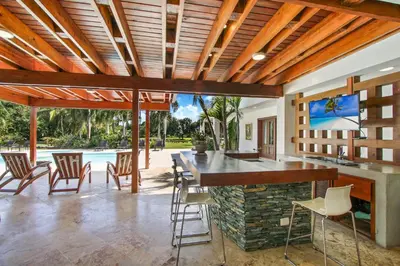 an outdoor kitchen with a bar with chairs and a pool at Casa de Campo villa – Luxurious villa up to 12 people with pool jacuzzi golf in La Romana