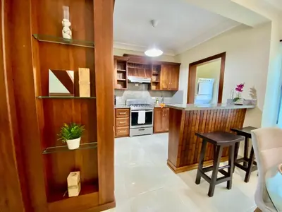 a kitchen with wooden cabinets and a table with a stool at Apartamento tipo hotel WIFI - Estacionamiento in Punta Cana